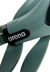 Gafas de natación de silicona verde suave con correa texturizada, que presentan un acento negro y logotipo. Las lentes están tintadas para reducir el deslumbramiento.