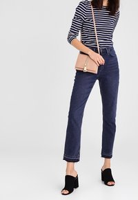 Pasiasta koszula z długim rękawem, ciemnoniebieskie jeansy z wysokim stanem, czarne szpilki z odkrytymi palcami oraz mała różowa torba na ramię. Minimalistyczny design.