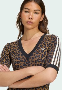 Polo majica s uzorkom leoparda, kratkim rukavima, V-izrezom, crnim detaljima i tri bijele pruge duž ramena. Materijal je mješavina pamuka.