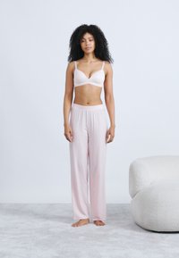 Light pink wireless bra with smooth cups paired with loose, patterned pajama pants in a similar shade, featuring an elastic waistband.