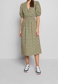 Květinové šaty s nafouknutými rukávy, elastickým pasem a délkou ke kolenům. Nosené s barevnými teniskami s akcenty v zelené, růžové a bílé barvě.