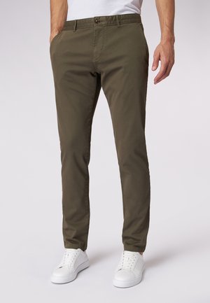 Chinos verde oliva con vestibilità slim, realizzati in un morbido misto cotone, dotati di chiusura frontale con bottone e tasche laterali. Abbinati a sneaker bianche.