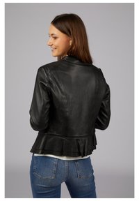 Black leather jacket with a fitted design and peplum detail at the hem, paired with blue jeans. The finish is smooth, with minimal hardware.