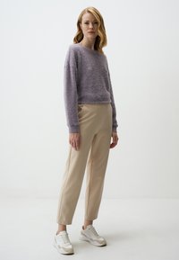 Maglione viola chiaro e peloso, pantaloni beige su misura e sneakers bianche. Texture morbide, vestibilità rilassata e design sportivo con accenti delicati.