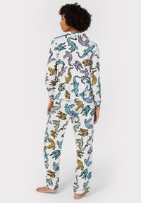 Pyjamaset med långärmad tröja och byxor, på vit bakgrund, med färgglada djurmotiv i blått, grönt, gult och lila. Mjuk tyg, lös passform.