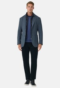 Granatowa marynarka z mieszanki wełny na czarnej pikowanej kurtce, w połączeniu z granatowym swetrem i czarnymi sztruksowymi spodniami, do tego czarne trampki.