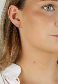 Guldörhänge med en liten klar ädelsten som accent. Enkel design, slät yta och polerat finish, bärs i örat.