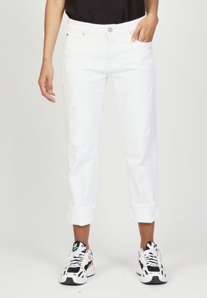 White denim jeans with distressed detailing, cropped cuffs, and a classic five-pocket design, paired with black and white sneakers.
