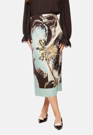 Woman wearing a high-waisted midi skirt with large floral print in brown, beige, and light blue, paired with brown blouse and two-tone pointed shoes.