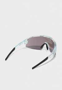Lunettes de soleil avec une monture en plastique transparent et des branches en caoutchouc noir, dotées de verres teintés foncés et d'un design aérodynamique qui épouse la forme du visage.