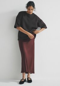 Oversized czarny t-shirt, burgundowa satynowa spódnica maxi i czarne baleriny. Gładka tekstura, luźny krój i minimalistyczny design z krótkimi rękawami.