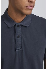 Námořnické polo tričko vyrobené z texturované látky, s límečkem, dvěma černými knoflíky a krátkými rukávy.