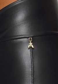 Czarna spódnica z materiału ekologicznego z dekoracyjnym akcentem w postaci złotej pszczoły i pionowymi przeszyciami. Gładka tekstura i dopasowany krój.