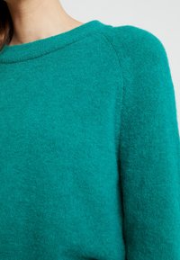 Turkusowy sweter dzianinowy z okrągłym dekoltem, miękką teksturą i raglanowymi rękawami, prezentujący przytulny wygląd z lekko luźnym krojem.