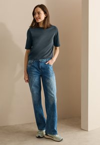 Šedý krátký rukáv top, světle modré vybledlé džíny s kapsami a béžové tenisky. Hladká textura a uvolněný střih. Jednoduchý design.