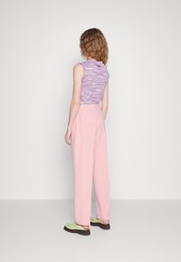 Haut sans manches ajusté violet et rose associé à un pantalon rose taille haute et des chaussures vertes à enfiler. Textures simples et lisses, lignes épurées.