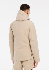 Beige Kapuzenjacke mit glatter Textur, geradem Schnitt, minimaler Detailgestaltung und einem Logostick auf der Seite in der Nähe des Saums.
