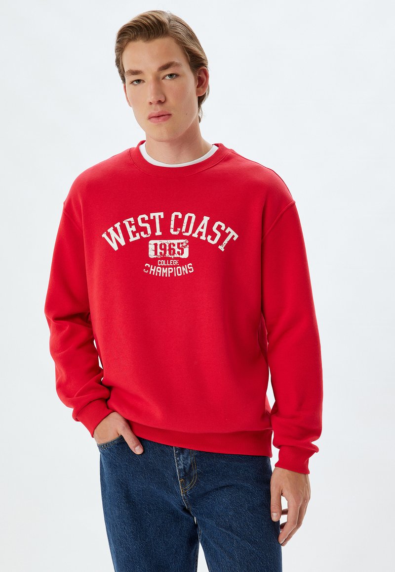 Sudadera de cuello redondo roja con un estampado vintage blanco que dice "CAMPEONES DE LA UNIVERSIDAD DE LA COSTA OESTE 1965", con puños y dobladillo acanalados.