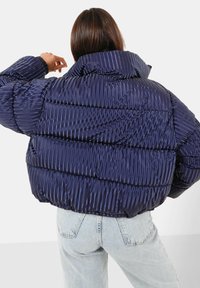 Giacca blu navy imbottita con texture a coste, colletto alto e maniche lunghe, caratterizzata da sezioni a righe orizzontali e polsini elasticizzati.
