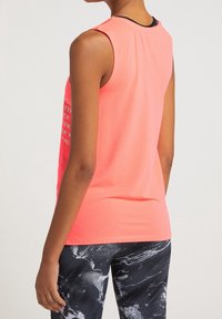 Top sportivo senza maniche di colore rosa, realizzato in tessuto morbido, con un audace design di testo bianco. Abbinato a leggings a motivo bianco e nero.