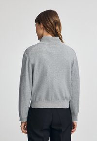 Pullover grigio lavorato a maglia con colletto alto, polsi e orlo a coste, e una texture morbida. La parte posteriore presenta una finitura liscia senza pattern visibili.