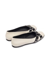 Ballerine in pelle crema con una fascia incrociata nera decorata con borchie argentate. Punta rotonda e suola piatta, progettate per il massimo comfort.
