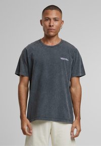 Čierna šedá prešitá tričko s okrúhlym výstrihom a krátkymi rukávmi. Obsahuje malé fialové logo na ľavej strane hrude. Mäkko štruktúrovaná látka.