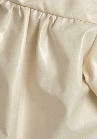 Tissu texturé beige clair, parsemé de paillettes métalliques argentées, avec des plis froncés. Surface lisse avec un léger éclat.