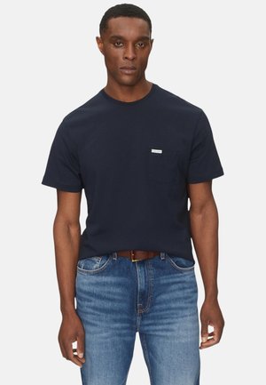 Maglietta a maniche corte color blu navy con scollo rotondo e una piccola tasca sul petto. Abbinata a jeans di denim azzurro chiaro e cintura marrone.