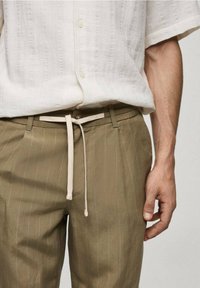 Lehká, texturovaná bílá košile s krátkým rukávem nošená přes olivově zelené kalhoty s proužky, se béžovým stahovacím páskem a předními kapsami.