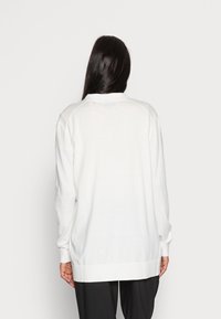 Biały sweter z długim rękawem, zakończony prążkowanym ściągaczem przy dolnej krawędzi i mankietach, o gładkiej fakturze i luźnym kroju. Brak widocznych wzorów ani akcentów.