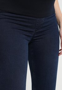Jeans de mezclilla azul oscuro con un corte ajustado. Presentan una cintura de altura media, costuras sutiles y una tela de textura suave. Sin hardware visible.