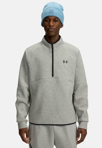 Gaišs pelēks zip-sviests ar melniem akcentiem un Under Armour logo; kopā ar gaiši zilā adītā cepure. Mīksta, teksturēta auduma.