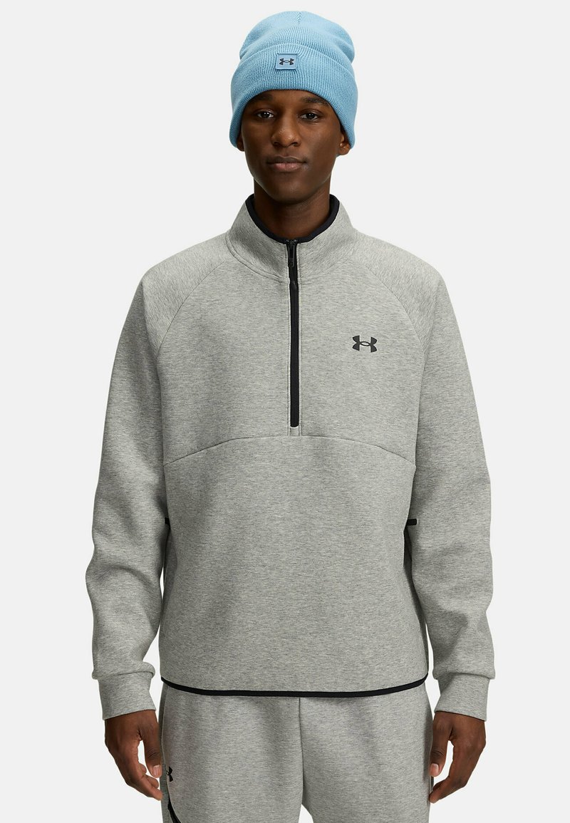 Gaišs pelēks zip-sviests ar melniem akcentiem un Under Armour logo; kopā ar gaiši zilā adītā cepure. Mīksta, teksturēta auduma.