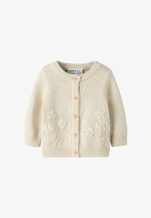 Kreemikarva kudumiskardigan ümar kaeluse, viie puidust nööbi ja esikülje lillelist tikandit. Soonilised varrukasääred ja alumine serv.