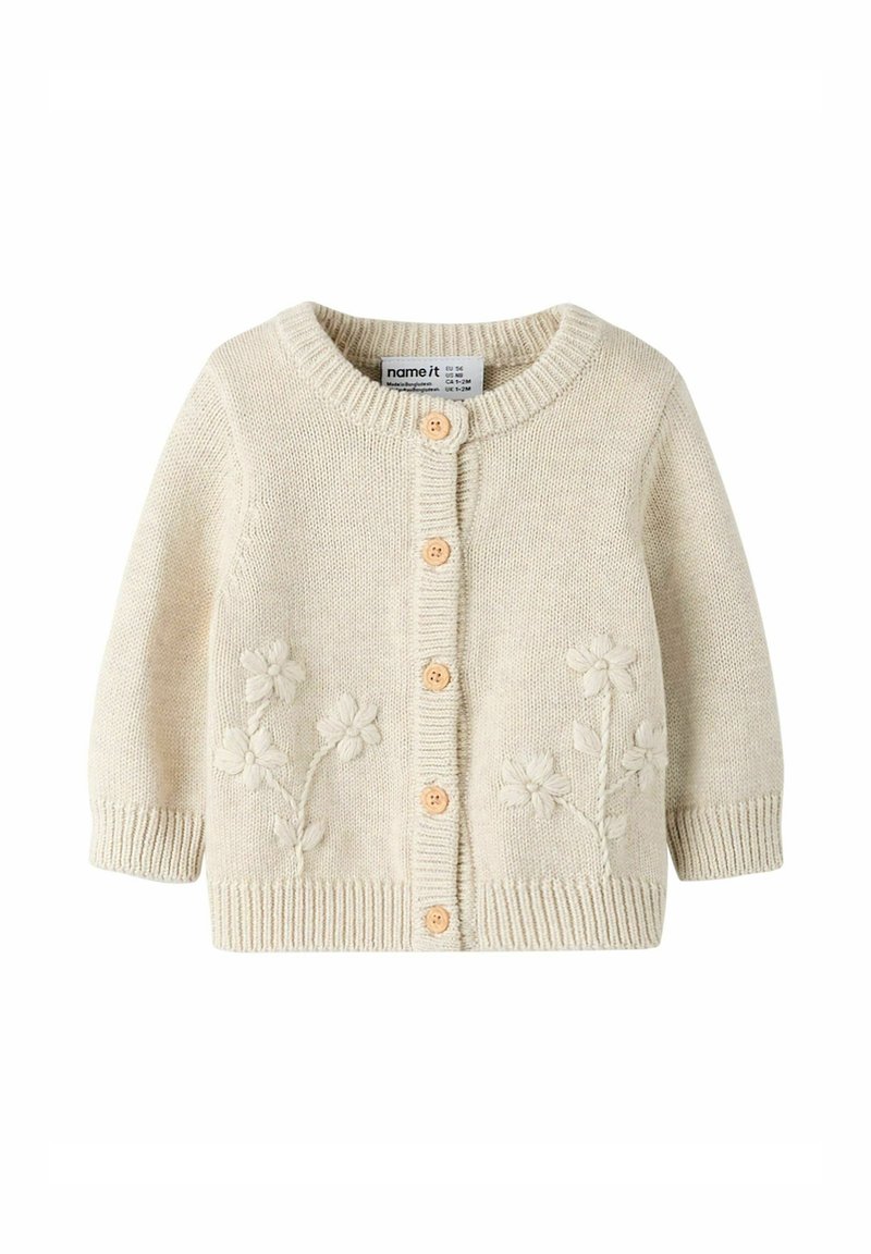 Kreemikarva kudumiskardigan ümar kaeluse, viie puidust nööbi ja esikülje lillelist tikandit. Soonilised varrukasääred ja alumine serv.