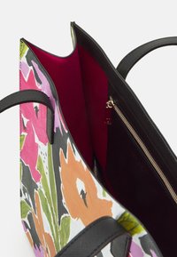 Stor axelremsväska med ett blommönster i rosa, orange och grönt på vit botten, med mörk svart texturfri läderdetaljer och en djupröd inredning.