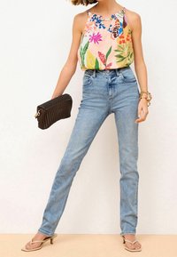 Květinový potisk bezramínkového topu v růžové barvě, světle modré džíny s vysokým pasem a béžové sandály na podpatku. Doplňky zahrnují tkanou tmavou kabelku.