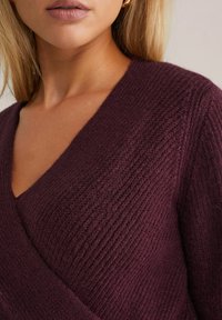 Pull en tricot bordeaux avec un décolleté en V profond, arborant un motif texturé. Matière douce et chaude avec une coupe décontractée et un design enveloppant.