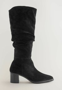 Zwarte suède kniehoog laars met een slouchy ontwerp, voorzien van een chunky hak en een gladde, gestructureerde afwerking. Geen zichtbare hardware of accenten.