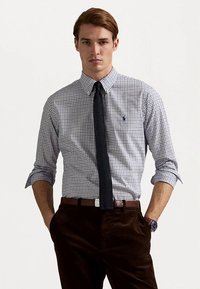 Koszula zapinana na guziki w niebiesko-białą kratę, długie rękawy podwinięte, z granatowym krawatem i brązowymi sztruksowymi spodniami. Logo Polo na piersi.