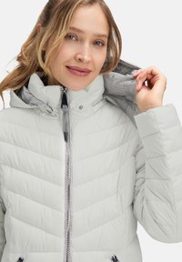 Jasnoszara kurtka puchowa z wzorem w zygzak, zapinana na zamek, z regulowanym kapturem oraz szarym podszewką. Posiada metalowe okucia zamka i boczne kieszenie.