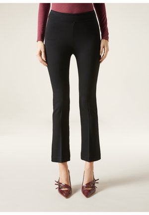 Pantalones acampanados negros con una textura de tela suave y un cinturón de altura media, combinados con tacones marones de punta afilada con detalles de correas.