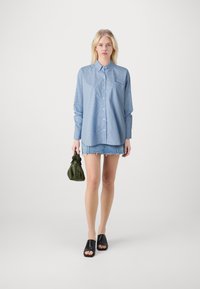 Svetlo modra prugasta srajca z gumbi in žepom, v kombinaciji z denim mini krilom, črnimi čevlji z odprtimi prsti in zeleno torbico.
