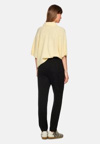 Gelber Strickpullover mit Kragen, kombiniert mit schwarzen Jogginghosen mit Muster. Der Look wird mit Sneakers im Animal-Print abgerundet.