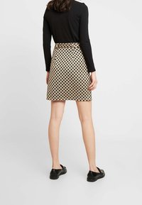 Falda de lunares en beige con puntos negros, de longitud hasta el muslo, con una cinturilla y diseño de cinturón. Combinada con un top negro de manga larga y zapatos negros.