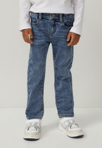 Jeans in denim blu medio con design a gamba dritta, cinque tasche e cuciture a contrasto, abbinati a sneakers bianche sportive.