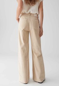 Beige Corduroy-Hosen mit weitem Bein, die eine senkrechte Rippstruktur, einen hohen Bund und zwei Gesäßtaschen zeigen, ergänzt durch ein dezent angebrachtes Taillenschild.