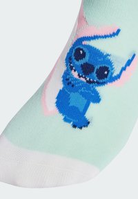 Calzino blu con un personaggio dei cartoni animati dai grandi occhi e un ampio sorriso, su uno sfondo verde menta con accenti rosa.