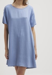 Vaaleansininen farkkuinen mekko, jossa on pyöreä pääntie, lyhyet hihat ja rento istuvuus. Mekossa on raakoja reunoja ja polvipituinen helma.